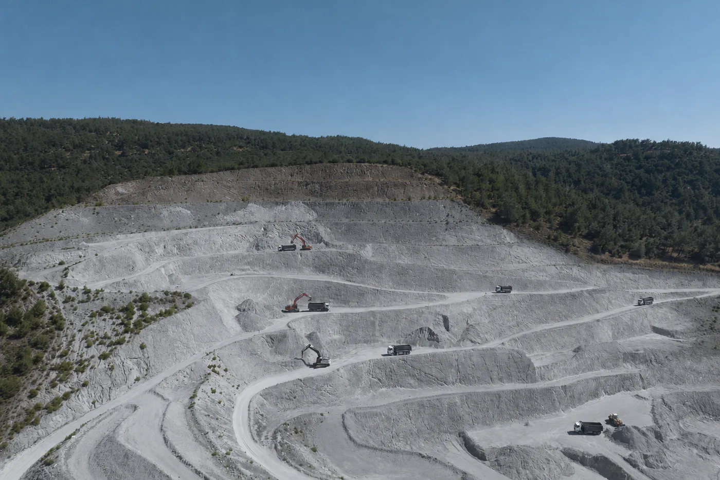 Aerial view of a terraced perlite quarry with haul trucks on the benches