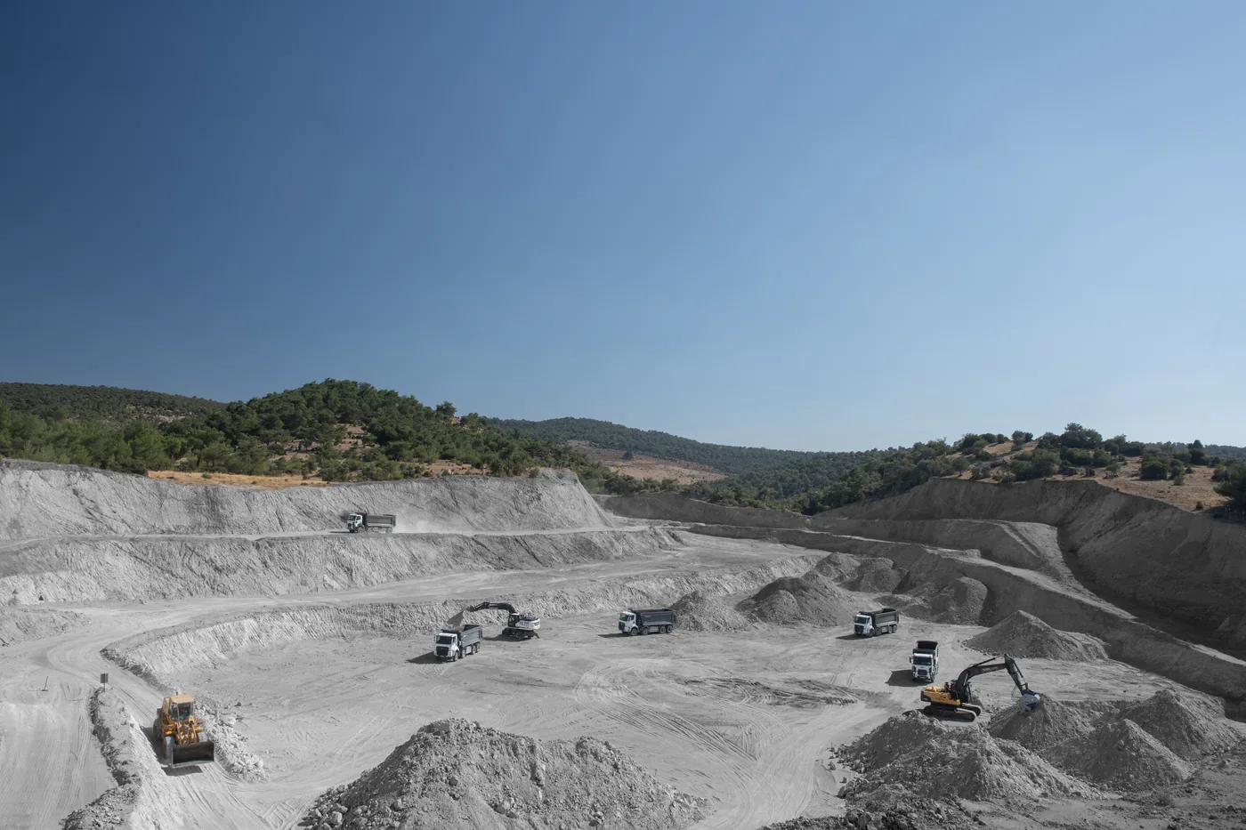 Excavators and haul trucks working the floor of an open-pit perlite quarry