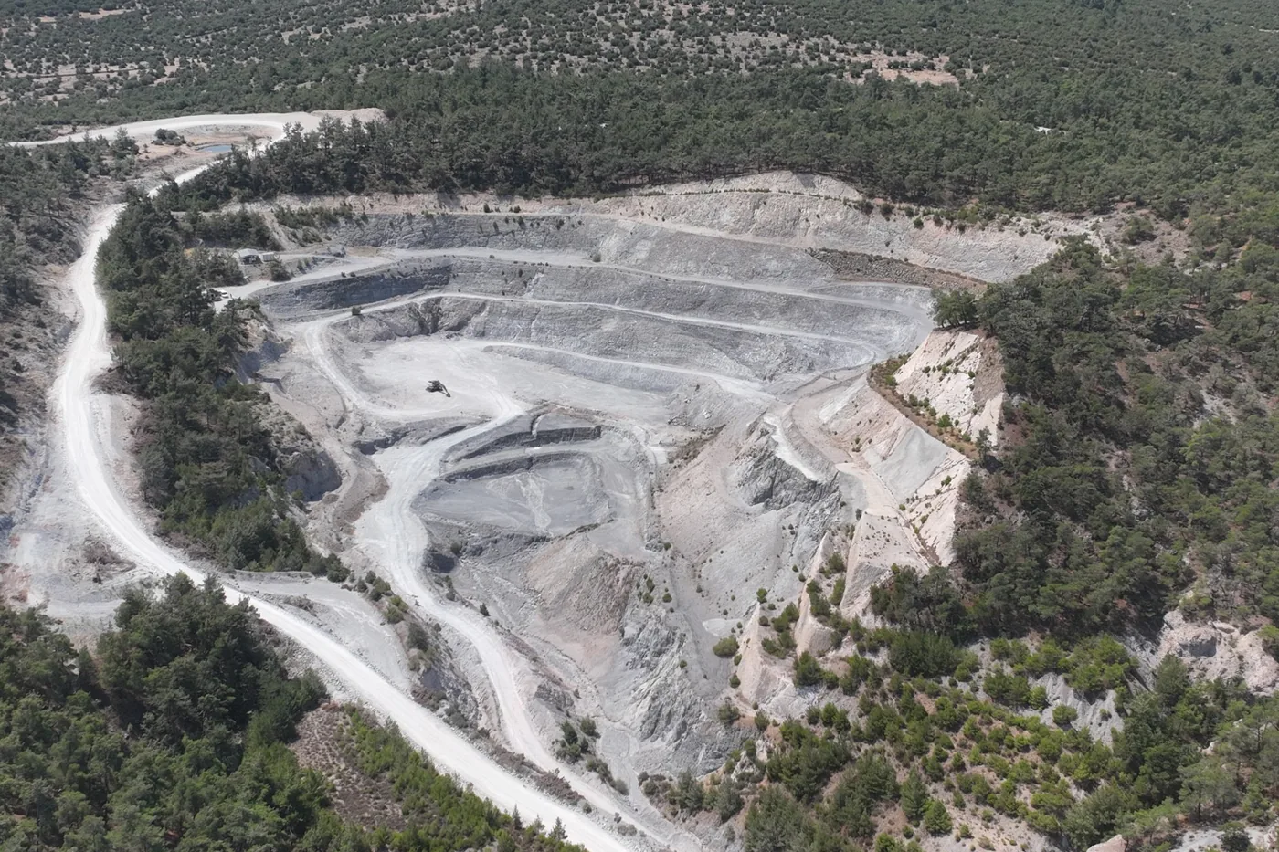 Aerial view of a benched perlite quarry and haul road surrounded by forest