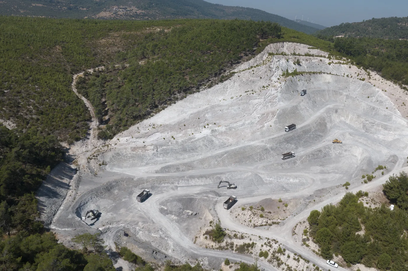 Aerial view of a perlite quarry on a forested hillside with machinery on the benches